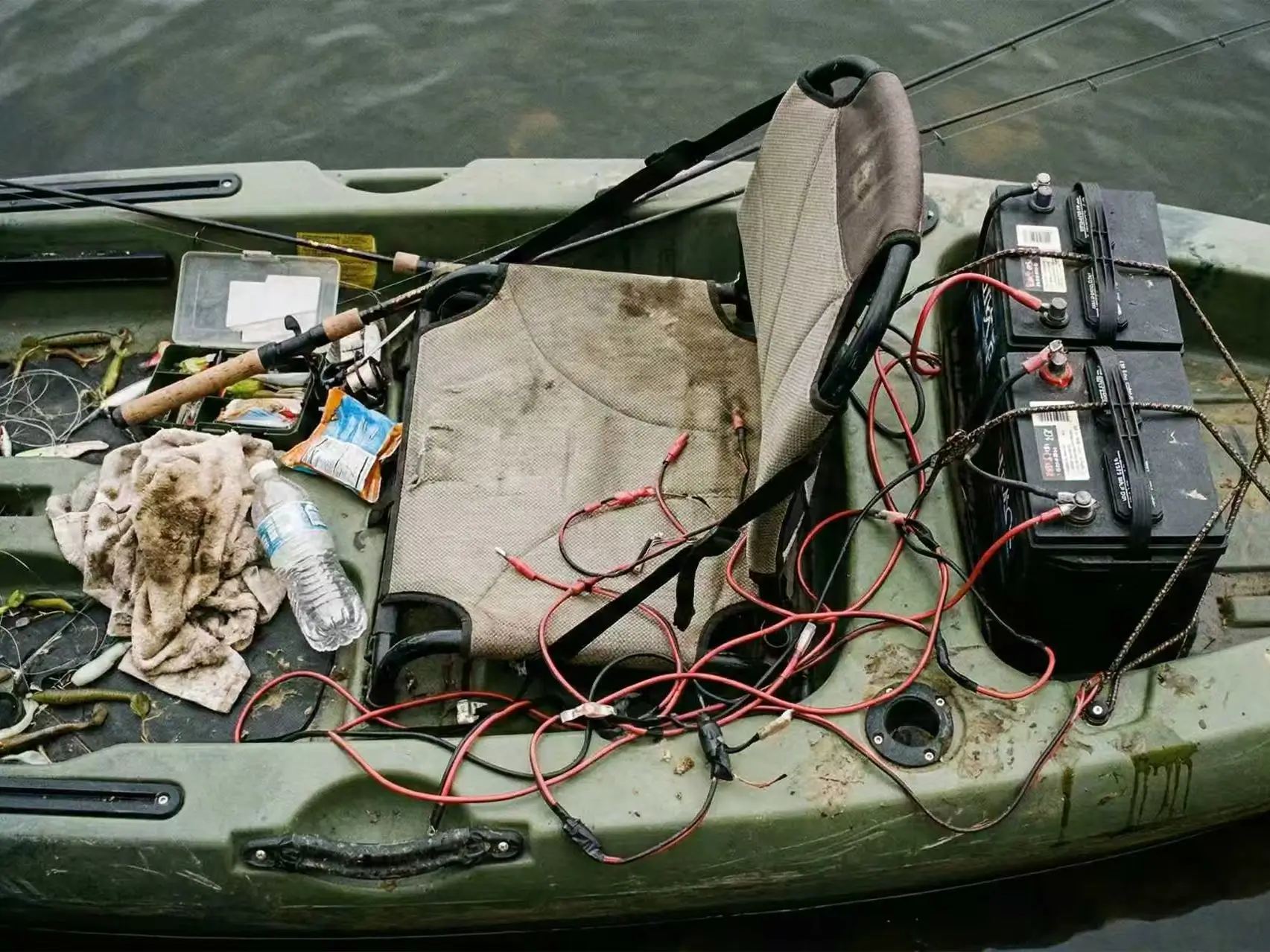 A cluttered kayak deck showing the messy exposed wires and heavy batteries typical of traditional DIY 24V trolling motor setups.