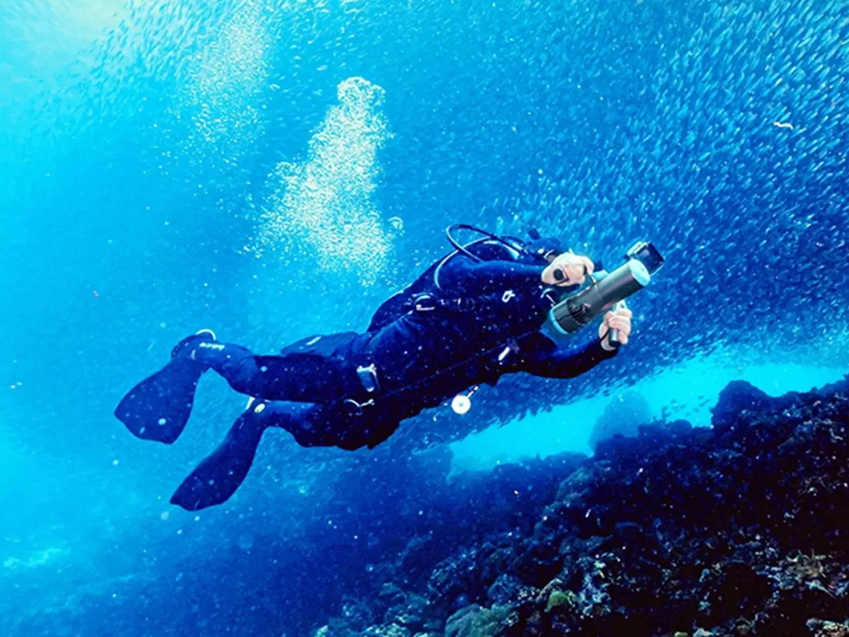 A freediver using the Tedgix K5 underwater scooter to explore a vibrant coral reef in clear blue water.