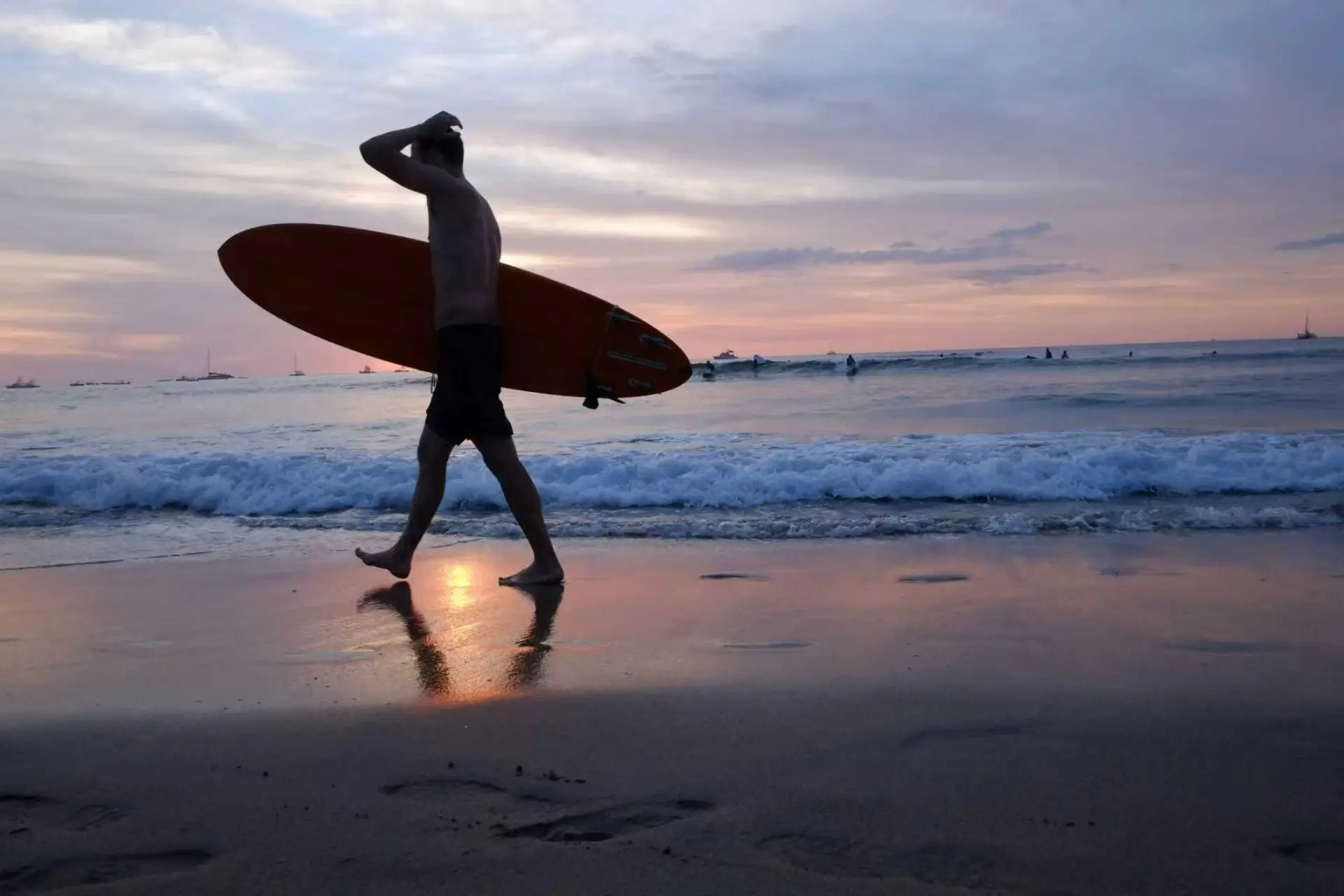 Silhouette of a surfer carrying their board walking along the beach at sunset, capturing the bohemian and tranquil vibe of Santa Teresa.
