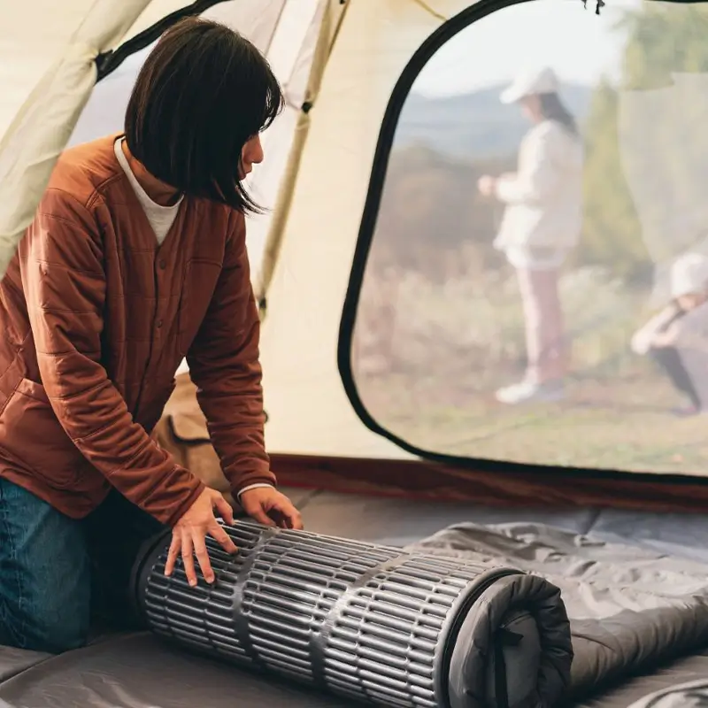 Camper rolling up a deflated sleeping pad inside a tent, showing how TEDGIX TurboBean helps with easy packing.
