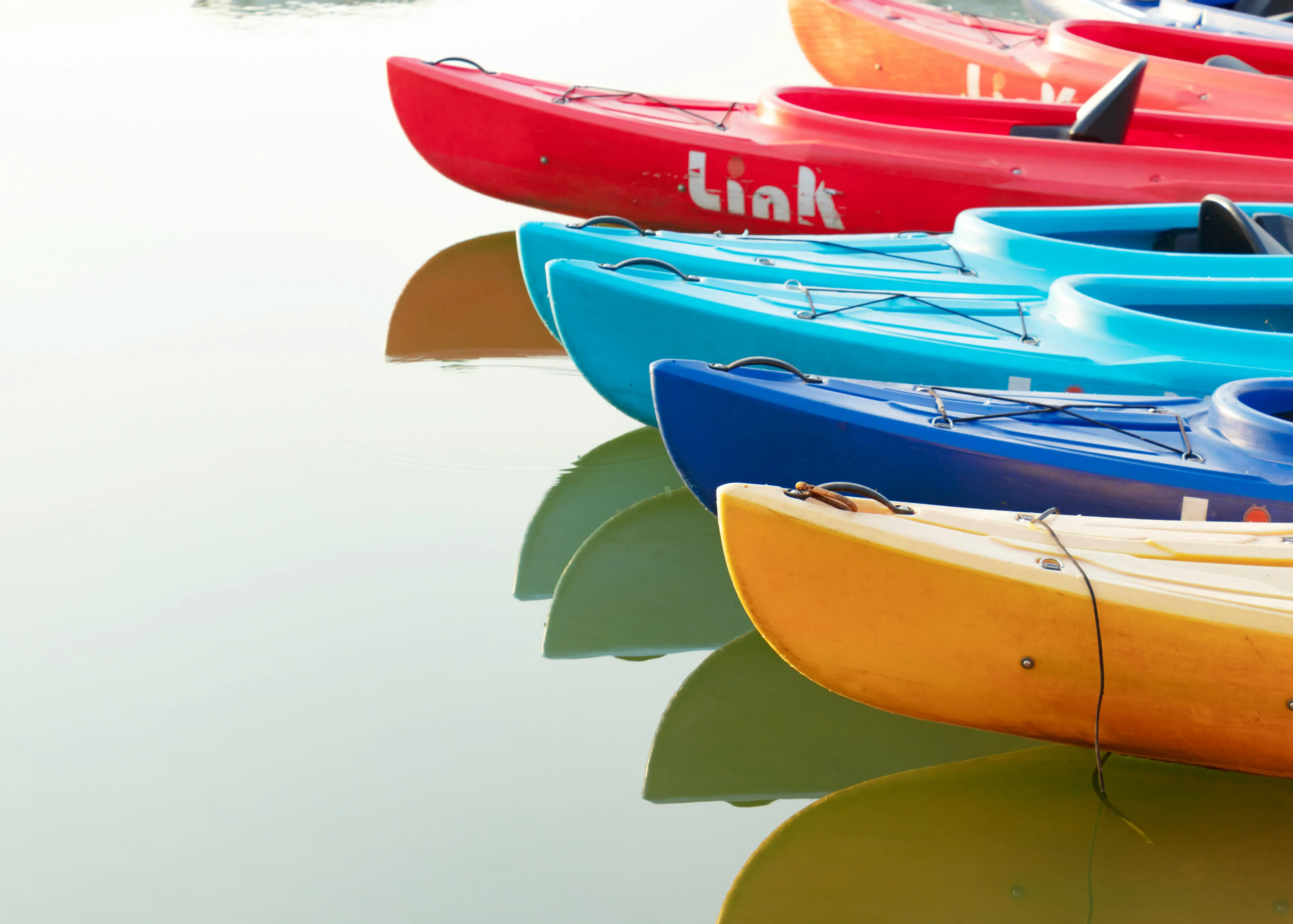 Different kayak hull designs aligned on water, showing platform variety and shape differences