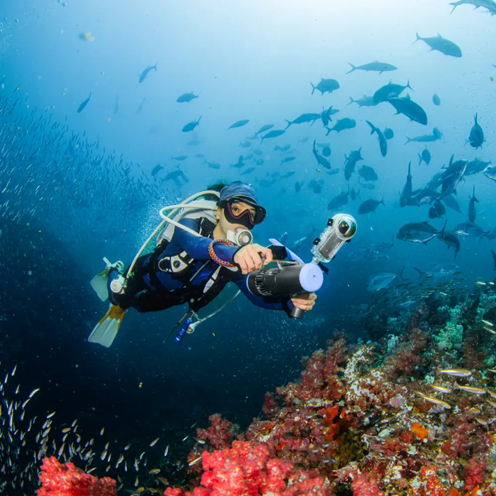 Diver exploring a vibrant coral reef using the handheld EDGE K5 underwater scooter with an action camera attached, surrounded by schools of fish. Ideal for scuba diving and snorkeling.